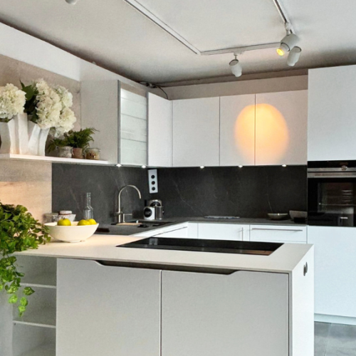 Cucina moderna bianca e nera con isola centrale, piano cottura, fiori bianchi e illuminazione design