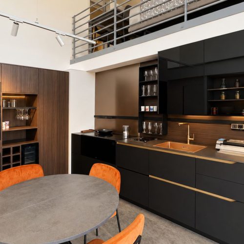 Cucina moderna Life con isola nera, tavolo rotondo e sedie arancioni in showroom