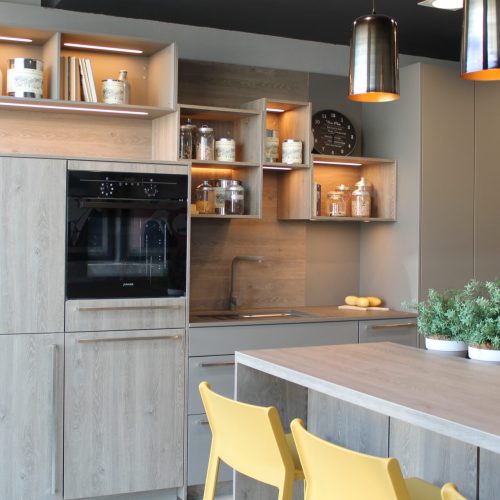 Cucina moderna con isola centrale, mobili in legno chiaro, mensole illuminate e sedie gialle.