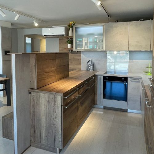 Cucina moderna showroom con isola in legno, elettrodomestici integrati e design contemporaneo.