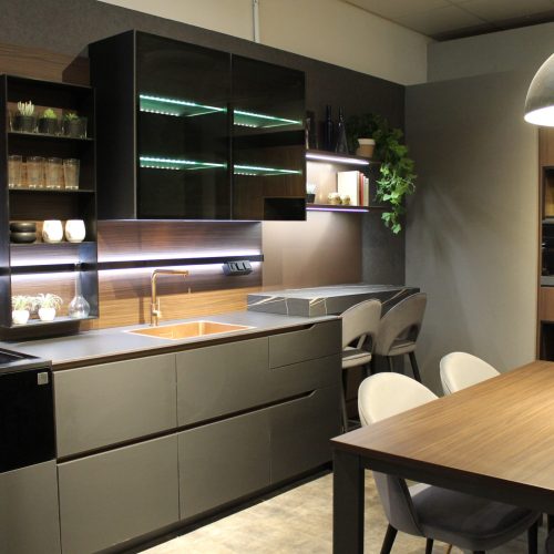 Cucina moderna con isola centrale, illuminazione LED verde, tavolo in legno e arredi eleganti in bianco e nero.