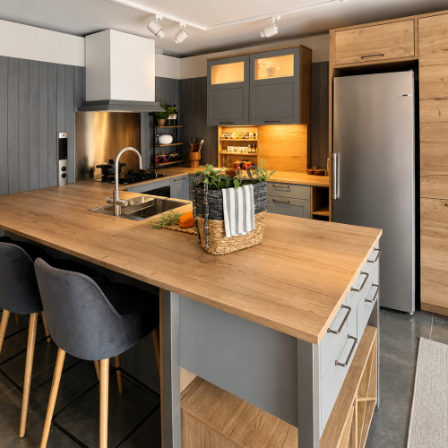 Cucina moderna con isola centrale in legno, sgabelli grigio-blu e cappe aspiranti sopra i fuochi a gas