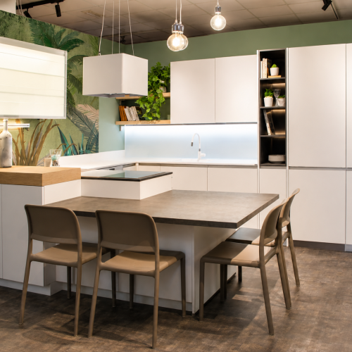 Cucina moderna bianca con isola, tavolo legno e sedie in stile nordico, parete verde con piante.