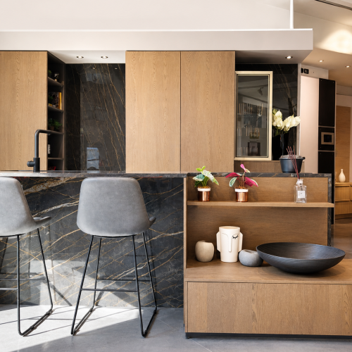 Cucina moderna con isola in marmo nero, sgabelli grigi e mobili in legno naturale di Life cucine italia.